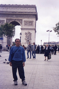 Our artist Low Hai Hong is a Singapore artist. ARTualize is the only art gallery in Singapore that represents him and his works.  A sixty year old Low Hai Hong standing in front of the Arc de Triomphe in Paris. Wearing a sweater, he looks on confidently.